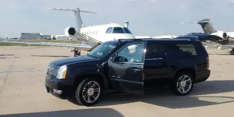 A black luxury SUV parked on an airport tarmac with a private jet in the background.