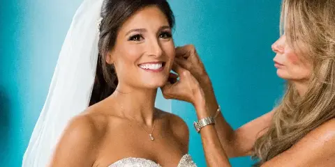 A makeup artist adjusting a bride's hair and makeup during a wedding preparation session.