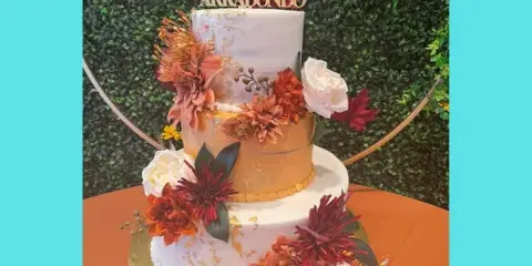 A three-tiered wedding cake with white and gold tiers, decorated with orange and red flowers and a Mr & Mrs topper.