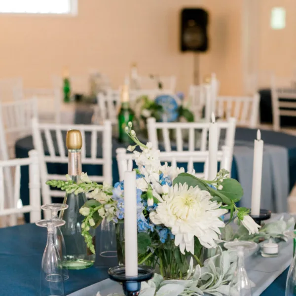 A wedding reception hall with white chairs, blue tablecloths, and floral centerpieces.