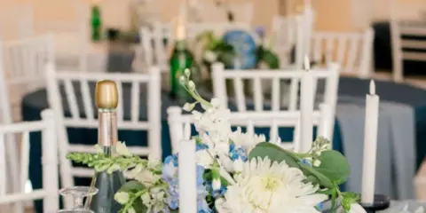 A wedding reception hall with white chairs, blue tablecloths, and floral centerpieces.