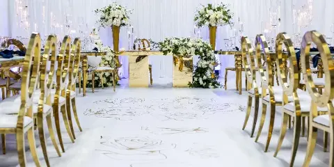A wedding reception setup featuring gold chairs, white floral arrangements, and a custom aisle runner.