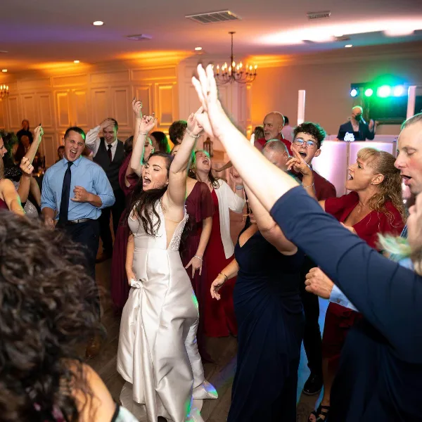 A bride and wedding guests dancing on a dance floor under colorful uplighting at a reception.