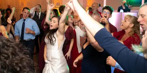 A bride and wedding guests dancing on a dance floor under colorful uplighting at a reception.