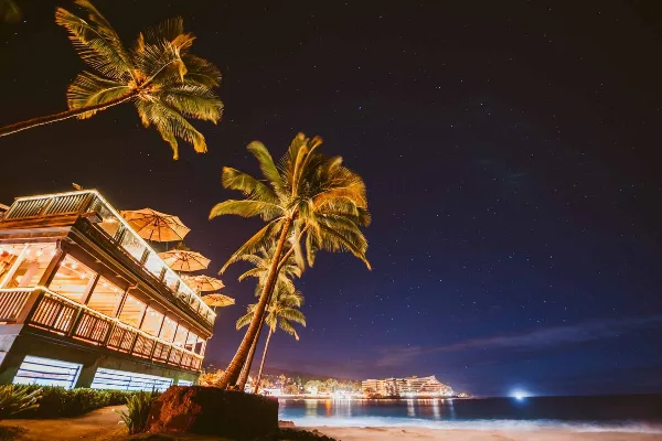 Nighttime exterior view of the Papa Kona Events & Catering oceanfront venue with palm trees and ocean view.