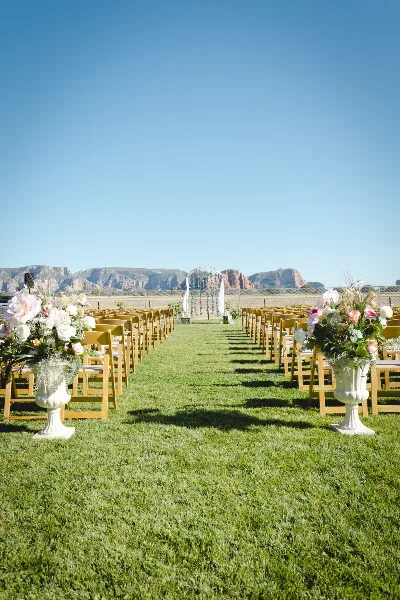 Outdoor wedding ceremony aisle with wooden chairs and floral arrangements on a lawn, with red rock buttes in the background.