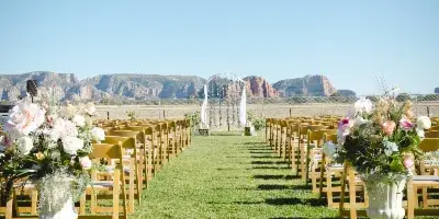 Outdoor wedding ceremony aisle with wooden chairs and floral arrangements on a lawn, with red rock buttes in the background.