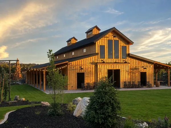 Exterior view of a large wooden barn event venue with a covered outdoor patio and string lights at dusk.