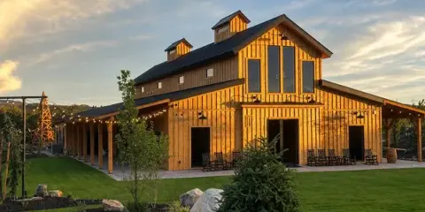 Exterior view of a large wooden barn event venue with a covered outdoor patio and string lights at dusk.