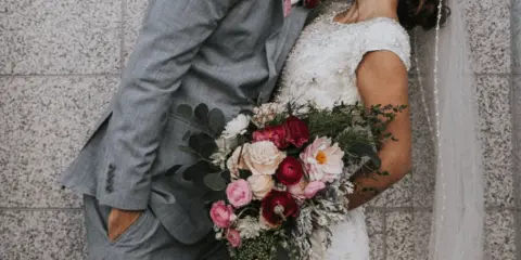 A bride and groom kissing while the bride holds a mixed floral bouquet and the groom wears a matching boutonniere.