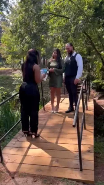 A wedding officiant performing a ceremony for a couple on a wooden bridge in a wooded area.