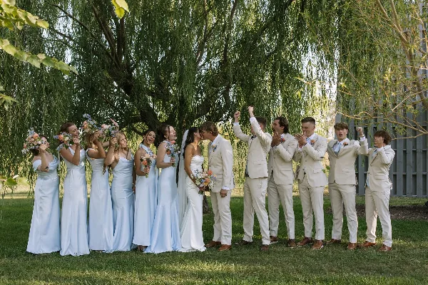 A wedding party including the bride and groom and their attendants celebrating outdoors under a large tree.