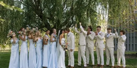 A wedding party including the bride and groom and their attendants celebrating outdoors under a large tree.
