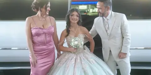 A woman in a formal gown and two other people standing in front of a luxury party bus.