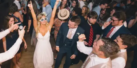 A bride and groom dancing on a crowded wedding dance floor surrounded by guests.