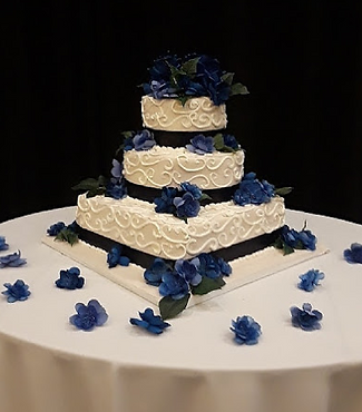 A three-tiered white wedding cake with textured frosting and blue floral decorations on a white table.