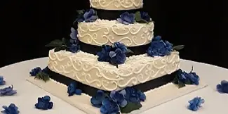A three-tiered white wedding cake with textured frosting and blue floral decorations on a white table.