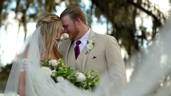 A bride and groom sharing a tender moment outdoors, with the bride holding a white bouquet and the groom wearing a beige suit.