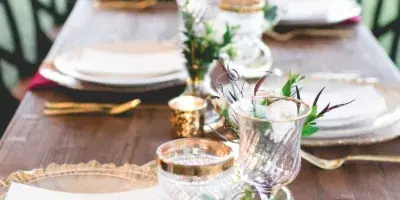 Elegant outdoor wedding reception table set with gold-rimmed plates, glassware, candles, and floral centerpieces.