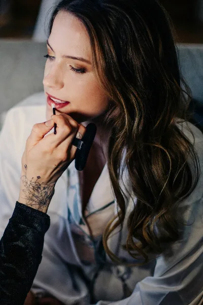 A makeup artist applying lip color to a client with long wavy hair.