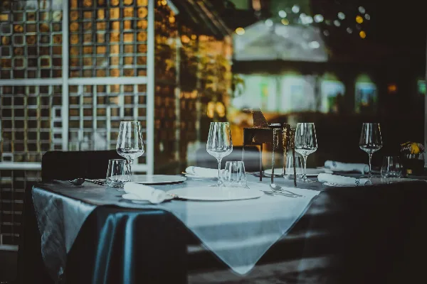 A professionally set dining table with white plates, wine glasses, and silverware on a dark tablecloth.