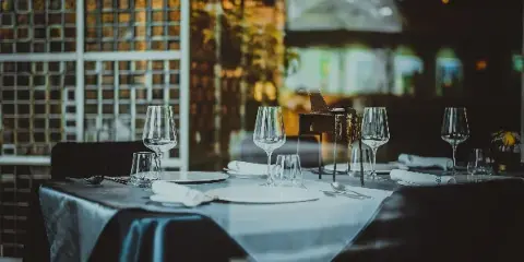 A professionally set dining table with white plates, wine glasses, and silverware on a dark tablecloth.