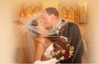A bride and groom kissing during a wedding ceremony with a bouquet of red flowers.