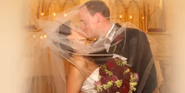 A bride and groom kissing during a wedding ceremony with a bouquet of red flowers.
