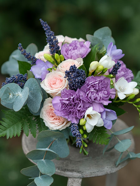 A close-up of a wedding floral arrangement with purple and pink flowers and greenery on a stone pedestal.
