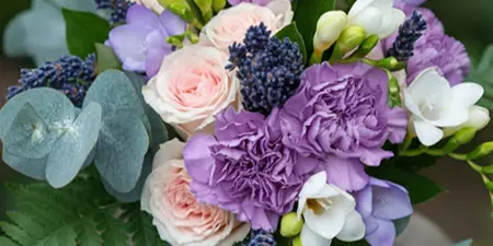 A close-up of a wedding floral arrangement with purple and pink flowers and greenery on a stone pedestal.