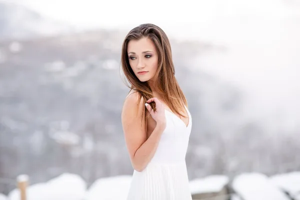 A professional portrait of a bride in a white dress standing outdoors with a blurred background.