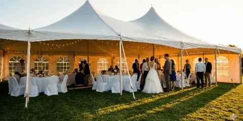 A white wedding tent set up on a lawn with a bride and groom and guests inside.