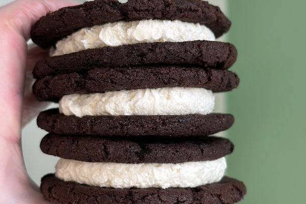 A hand holding a stack of chocolate cookies with white buttercream filling.