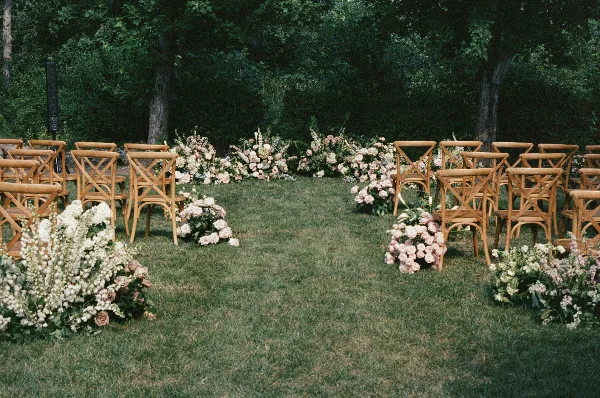 Outdoor wedding ceremony setup with wooden chairs and floral arrangements on a grassy lawn.