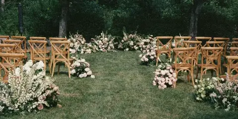 Outdoor wedding ceremony setup with wooden chairs and floral arrangements on a grassy lawn.