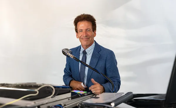 A professional DJ in a blue suit standing behind a mixing console and microphone.