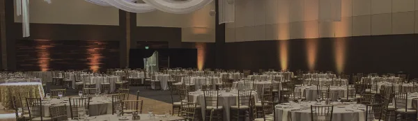 Interior of a large event hall set up for a wedding reception with round tables, chairs, and ceiling drapery.