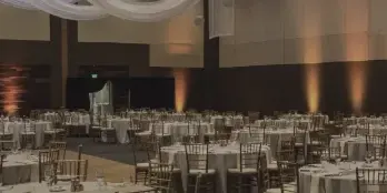 Interior of a large event hall set up for a wedding reception with round tables, chairs, and ceiling drapery.