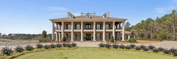 Exterior view of a two-story brick and stucco venue building with a large columned porch and manicured landscaping.