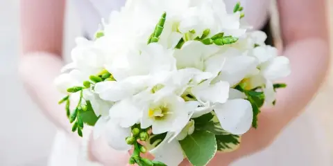 A bride holding a round bouquet of white flowers and greenery