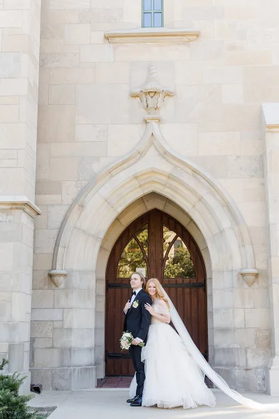 A bride and groom standing together in front of a stone church entrance.