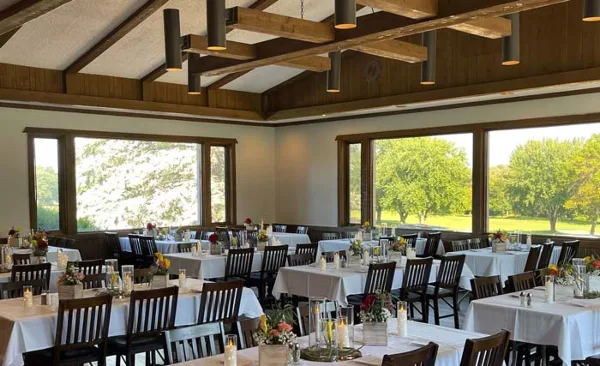An indoor wedding banquet hall with white tablecloths and large windows overlooking a green landscape.