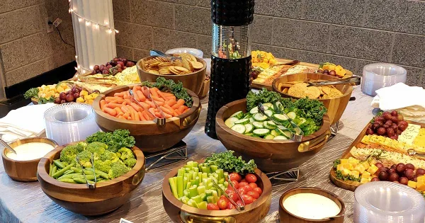 A catering buffet table set with wooden bowls containing fresh vegetables, cheese, and dips.
