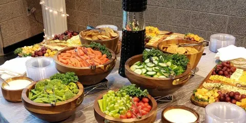 A catering buffet table set with wooden bowls containing fresh vegetables, cheese, and dips.