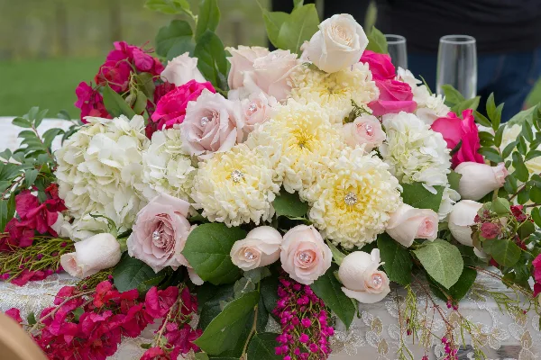 Elegant floral centerpiece with pink and white roses and chrysanthemums on a table with a lace runner.