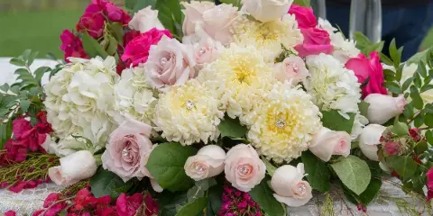 Elegant floral centerpiece with pink and white roses and chrysanthemums on a table with a lace runner.