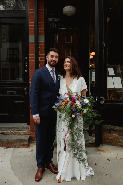 A bride and groom standing together in a doorway, with the bride holding a large bouquet.
