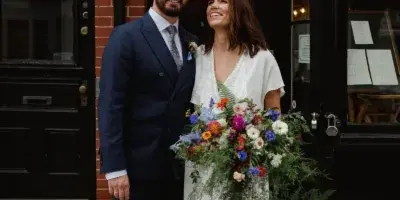 A bride and groom standing together in a doorway, with the bride holding a large bouquet.