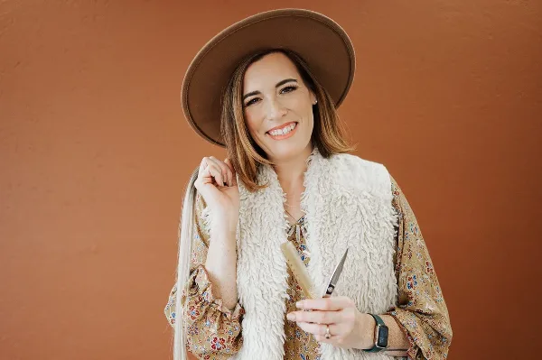 A smiling woman holding hairdressing scissors and a weft of hair extensions.
