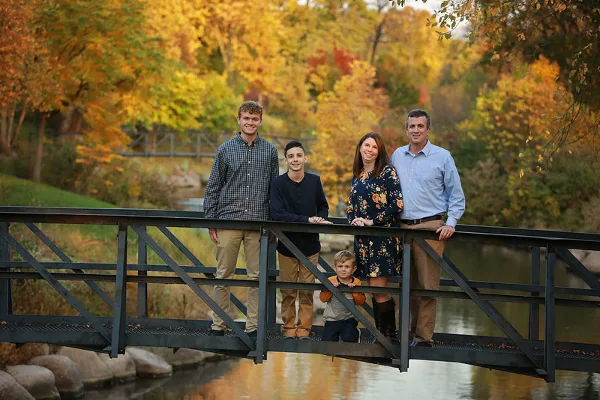A family of five posing on a metal bridge in a park with autumn foliage.